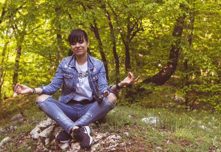 A woman meditates peacefully in a lush green forest, exuding calm and relaxation.