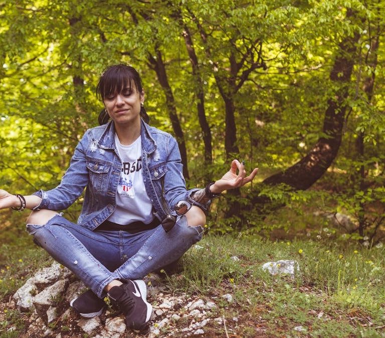 A woman meditates peacefully in a lush green forest, exuding calm and relaxation.